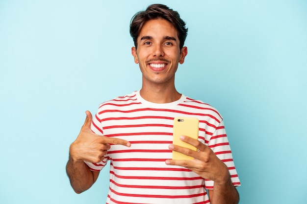 Junge gemischte Rasse Mann mit Handy isoliert auf blauem Hintergrund Person zeigt mit der Hand auf ein Hemd Kopie Raum, stolz und selbstbewusst