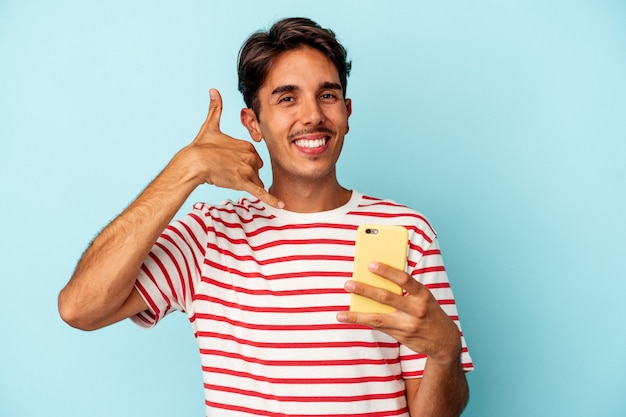 Junge gemischte Rasse Mann mit Handy isoliert auf blauem Hintergrund zeigt eine Handy-Anruf-Geste mit den Fingern.