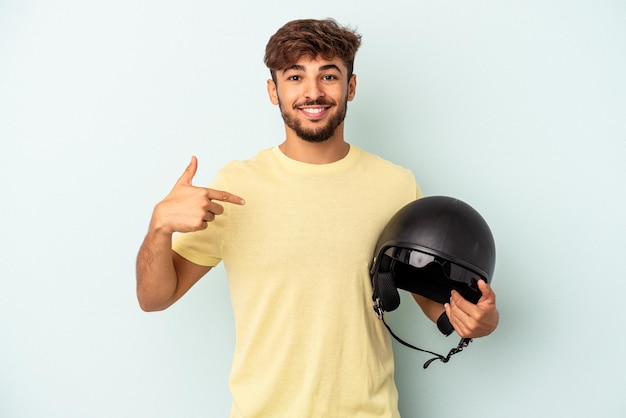 Junge gemischte Rasse Mann mit Motorradhelm isoliert auf blauem Hintergrund Person zeigt mit der Hand auf ein Hemd Kopie Raum, stolz und selbstbewusst