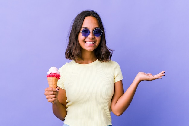 Junge gemischte Rassenfrau, die ein Eis isst, das einen Kopienraum auf einer Handfläche zeigt und eine andere Hand auf Taille hält.