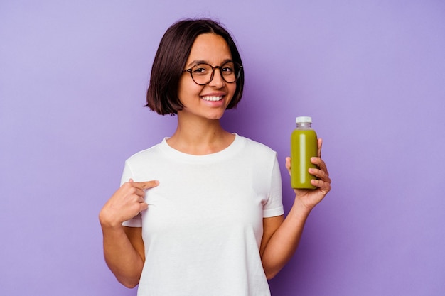 Junge gemischte Rassenfrau, die einen gesunden Smoothie lokalisiert auf lila Hintergrundperson hält, die von Hand auf einen Hemdkopierraum zeigt, stolz und zuversichtlich