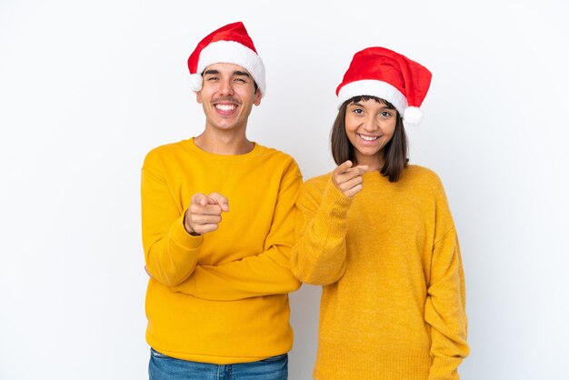 Junge gemischte Rassenpaare, die Weihnachten isoliert auf weißem Hintergrund feiern, zeigen mit einem selbstbewussten Ausdruck mit dem Finger auf Sie