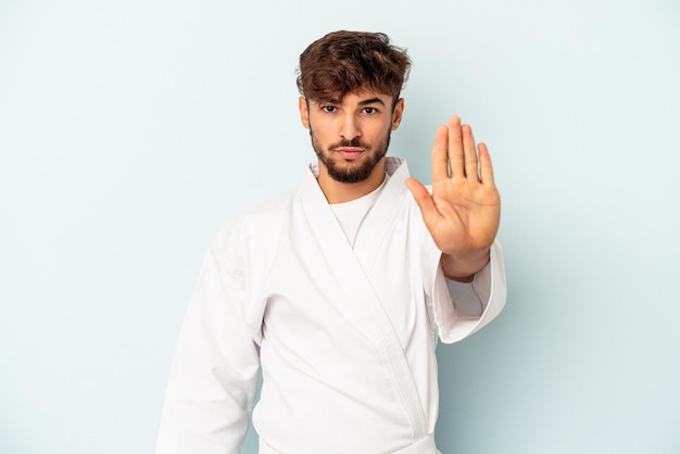 Junge gemischte Rennen Mann macht Karate isoliert auf blauem Hintergrund stehend mit ausgestreckter Hand mit Stoppschild und verhindert Sie.