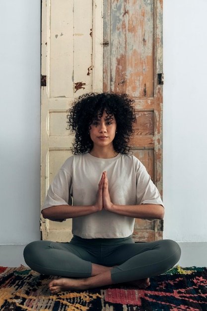 Junge gemischtrassige Frau, die auf dem Boden sitzt und mit den Händen im Gebet in die Kamera blickt Meditationskonzept Spiritualitätskonzept