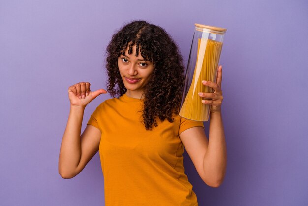 Junge gemischtrassige Frau, die Spaghetti einzeln auf violettem Hintergrund hält, fühlt sich stolz und selbstbewusst, Beispiel zu folgen.