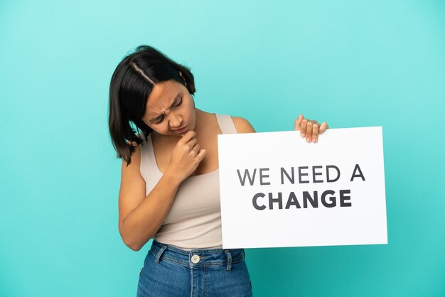 Junge gemischtrassige Frau isoliert auf blauem Hintergrund, die ein Plakat mit dem Text We Need a Change and Thinking hält