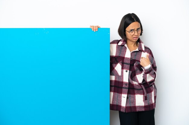 Junge gemischtrassige Frau mit einem großen blauen Plakat isoliert auf weißem Hintergrund, das auf sich selbst zeigt