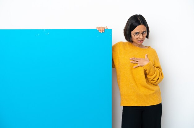 Junge gemischtrassige Frau mit einem großen blauen Plakat isoliert auf weißem Hintergrund, das auf sich selbst zeigt