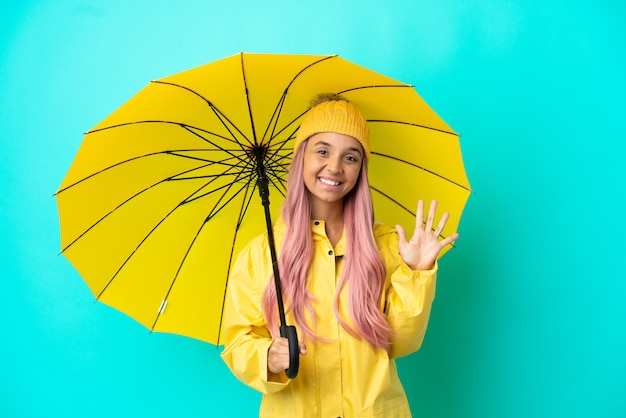 Junge gemischtrassige Frau mit regenfestem Mantel und Regenschirm, die mit den Fingern fünf zählt