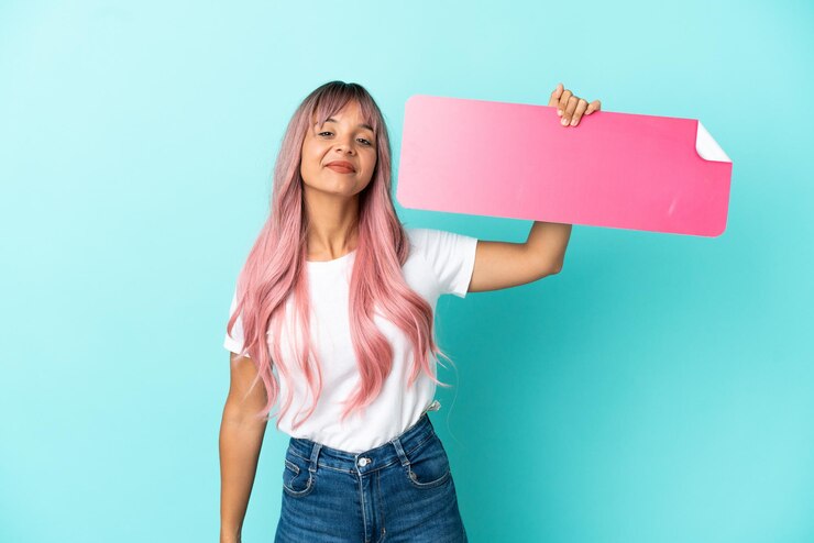Foto junge gemischtrassige frau mit rosa haaren auf blauem hintergrund isoliert, die ein leeres plakat hält