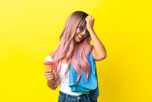 Junge gemischtrassige Frau mit rosa Haaren, die Eiscreme isoliert auf gelbem Hintergrund hält, hat etwas erkannt und beabsichtigt die Lösung
