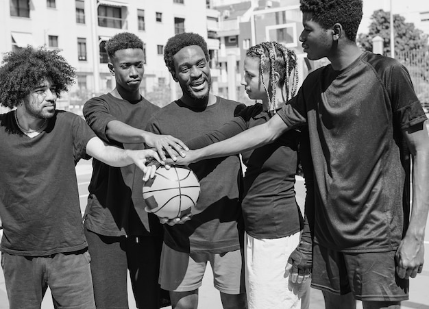 Junge gemischtrassige Menschen stapeln nach einem Sportmatch in der Stadt die Hände auf Basketball