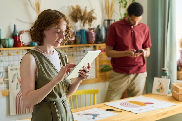 Junge gemischtrassige Mitarbeiter, die während der Arbeit im Studio mobile Gadgets verwenden