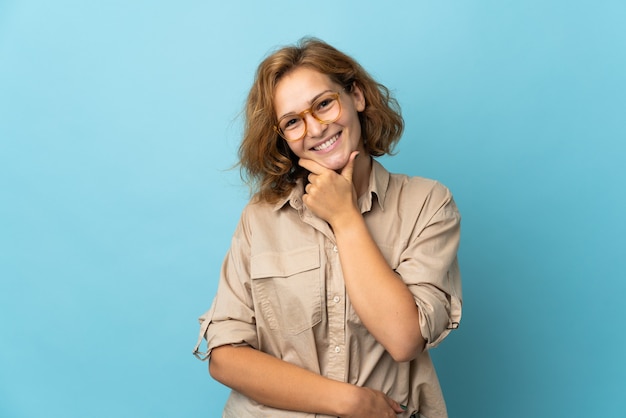 Junge georgianische Frau lokalisiert auf blauer Wand mit Brille und Lächeln