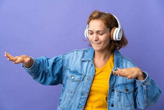 Junge georgische Frau lokalisiert auf lila Wand, die Musik hört und tanzt