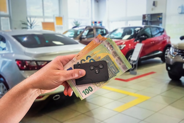 Junge, gepflegte Hände, die Euro-Banknoten und Autoschlüssel auf dem Hintergrund des Autos halten