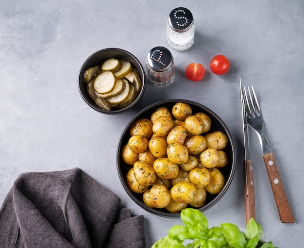 Junge geröstete Babykartoffeln in einer schwarzen Pfanne mit Tomaten und Gurken auf blauem Grund