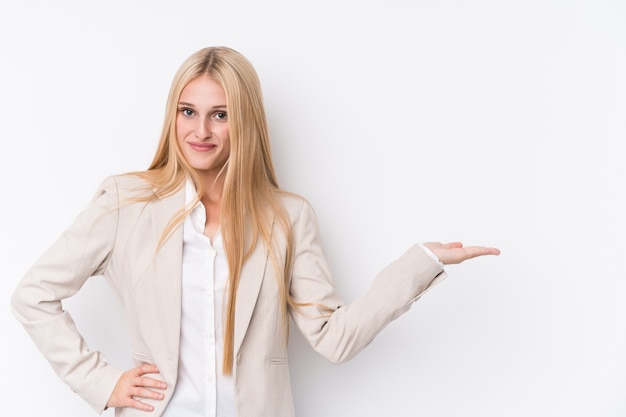 Junge Geschäftsblondine auf dem Weiß, das einen Kopienraum auf einer Palme zeigt und eine andere Hand auf Taille hält.