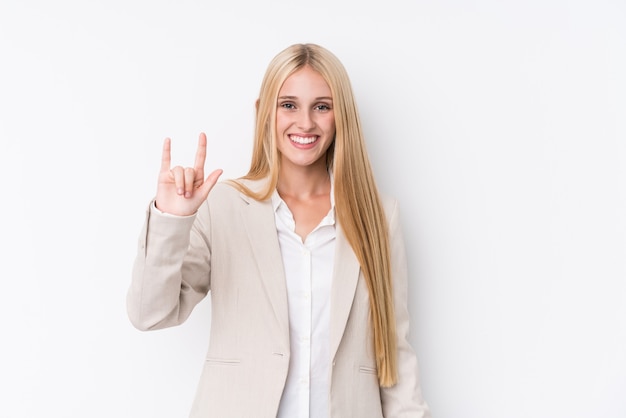 Junge Geschäftsblondine auf der weißen Wand, die eine Hörnergeste als Revolutionskonzept zeigt.