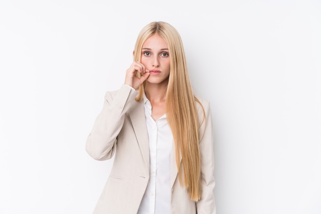 Junge Geschäftsblondine auf weißem Hintergrund mit den Fingern auf den Lippen, die ein Geheimnis halten.