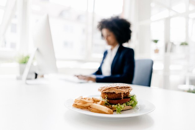 Junge Geschäftsfrau arbeitet mit Hamburger auf ihrem Schreibtisch