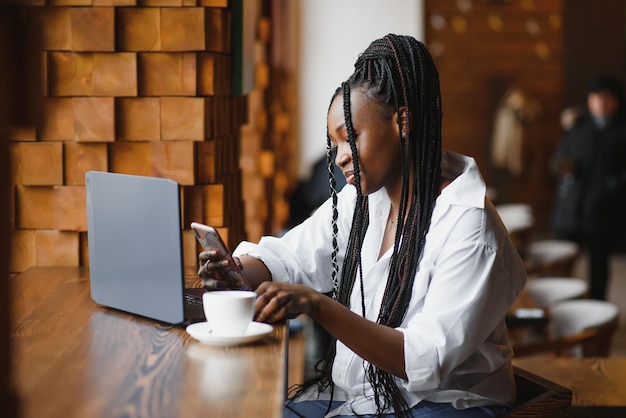 Junge geschäftsfrau arrangiert das nächste geschäftstreffen in einem modernen coworking space mit einem laptop junge freiberuflerin liest e-mails und andere nachrichten auf einem mobiltelefon