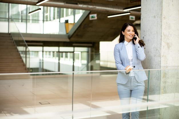 Junge Geschäftsfrau benutzt Mobiltelefon im Büroflur