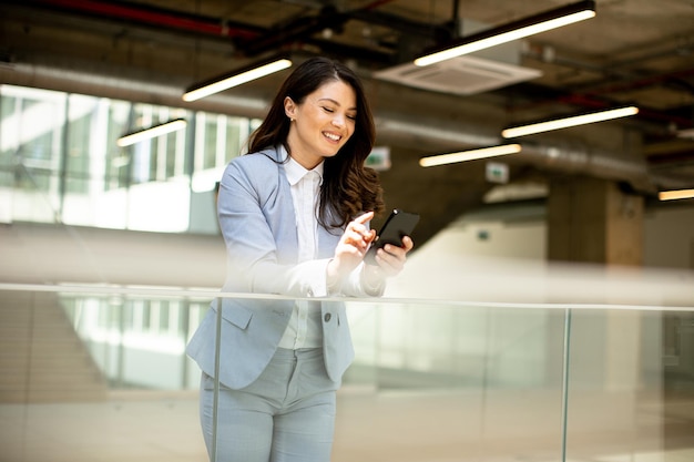 Junge Geschäftsfrau benutzt Mobiltelefon im Büroflur