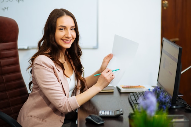 Junge Geschäftsfrau, die am Arbeitsplatz sitzt und Papier im Büro liest