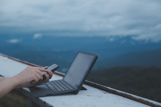 Junge Geschäftsfrau, die am Computer im Café auf dem Felsen arbeitet Junges Mädchen, das bei Sonnenuntergang oder Sonnenaufgang an einem Laptop arbeitet, auf dem Gipfel des Berges zum Meer Arbeitstag