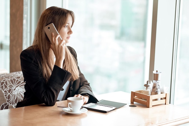 Junge Geschäftsfrau, die am Telefon im Kaffeegeschäft spricht