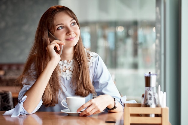 Junge Geschäftsfrau, die am Telefon im Kaffeegeschäft spricht