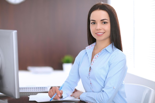 Junge Geschäftsfrau, die am Tisch im Büro sitzt und schreibt