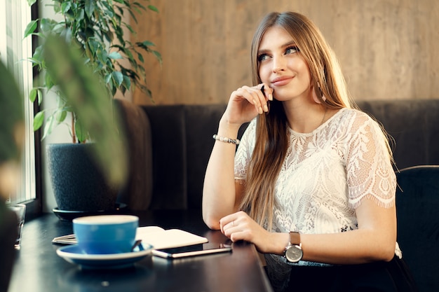 Junge Geschäftsfrau, die am Tisch in einem Kaffeegeschäft sitzt und Notizen macht