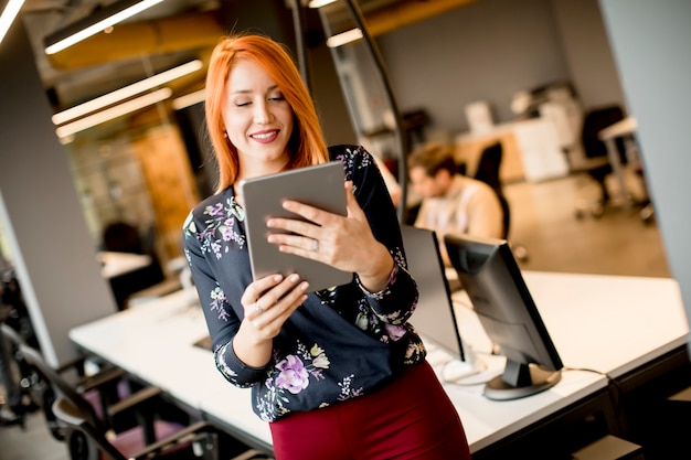 Junge Geschäftsfrau, die auf digitalem Tablett arbeitet, während im Hintergrundteam, das im modernen Büro arbeitet