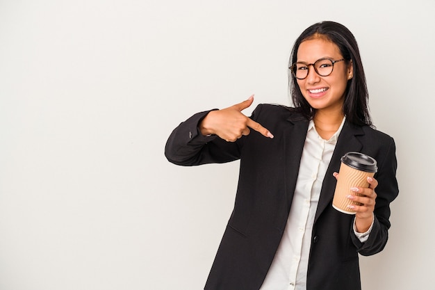 Junge Geschäftsfrau, die einen Kaffee zum Mitnehmen hält, isoliert auf weißem Hintergrund, der mit der Hand auf einen Hemdkopierraum zeigt, stolz und selbstbewusst