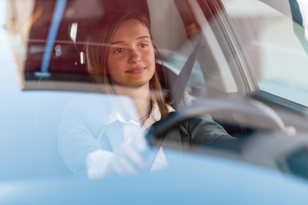 Junge Geschäftsfrau, die es genießt, auf Geschäftsreisen zu gehen und ein Auto zu fahren. Die Ansicht ist durch das Glas