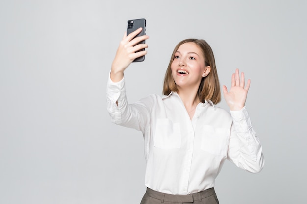 Junge Geschäftsfrau, die jemanden auf Videoanruf am Telefon auf weißer Wand begrüßt.