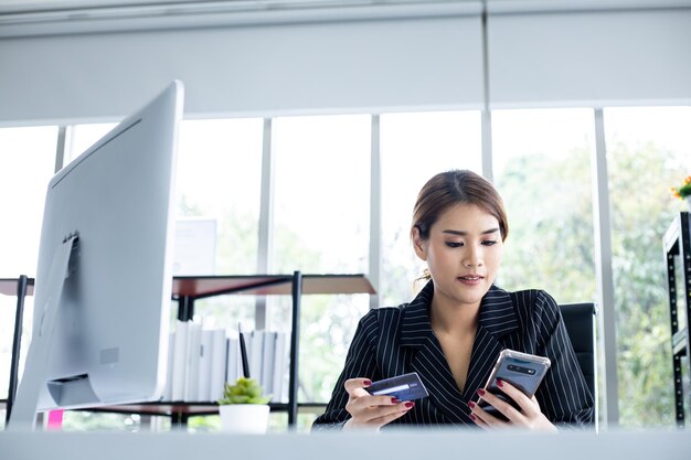 Junge Geschäftsfrau, die online über das Handy mit Kreditkarten einkauft, Rechnungen bezahlt, Produkte online mit glücklichem Arbeitszimmer bestellt. Online-Shopping, E-Commerce, Internet-Banking, Geld ausgeben.