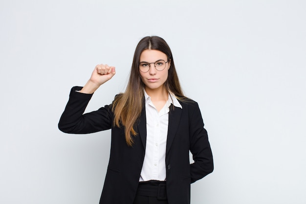 Junge Geschäftsfrau, die sich ernst, stark und rebellisch fühlt, die Faust erhebt, protestiert oder für die Revolution über der weißen Mauer kämpft