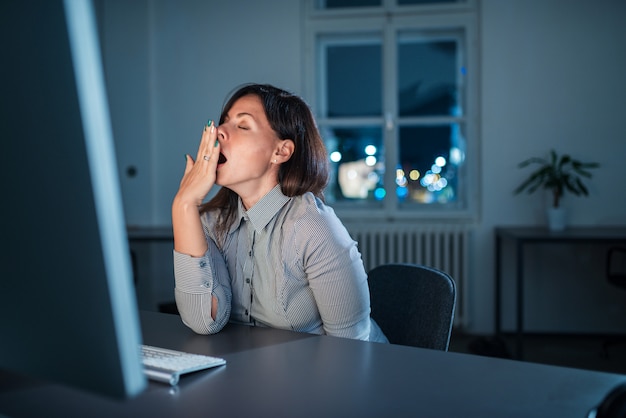 Junge Geschäftsfrau, die spät am Arbeitsplatz nachts gähnt.