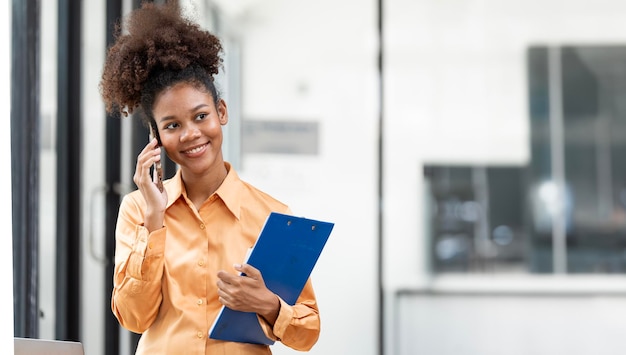 Junge Geschäftsfrau, fröhliche afroamerikanische Dame, die im Büro arbeitet und Dokumente in der Hand hält, während sie Platz für Telefongespräche hat