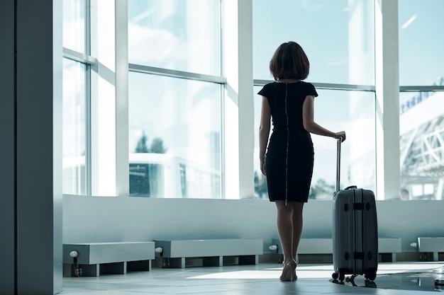 Junge Geschäftsfrau im Flughafen mit Gepäck, das auf Abfahrt wartet