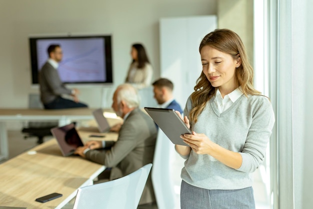 Junge Geschäftsfrau im Startbüro mit digitaler Tablette vor ihren Kollegen als Teamleiter