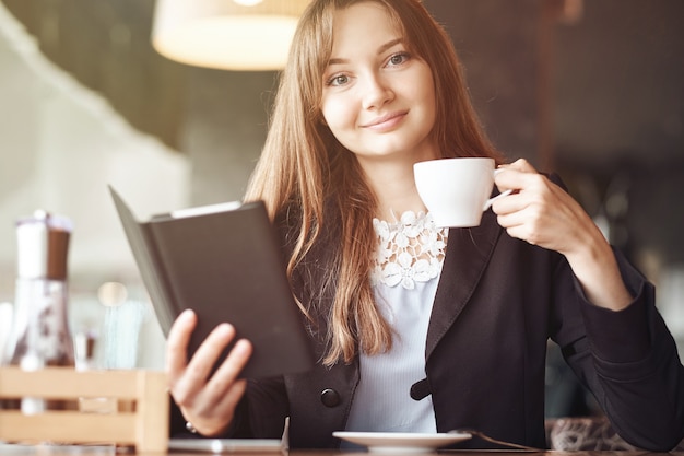 Junge Geschäftsfrau in einem Café, das ein ebook liest und Kaffee trinkt