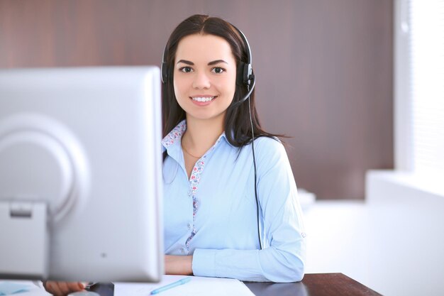 Foto junge geschäftsfrau in einem headset, das am tisch im büro sitzt