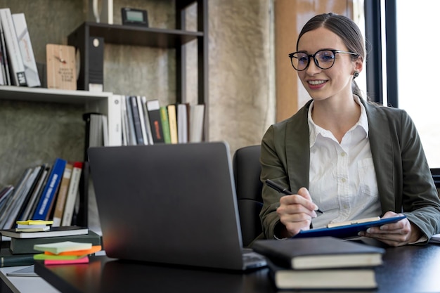 Junge Geschäftsfrau mit Brille, die im Büro an Dokumenten und Laptop-Computern arbeitet