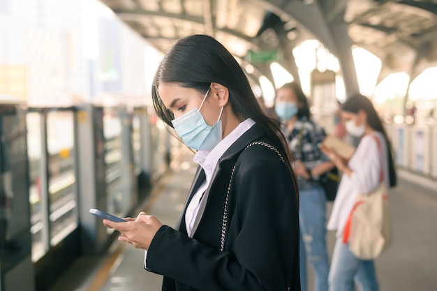 Junge Geschäftsfrau mit Gesichtsmaske steht auf U-Bahn-Plattform mit Smart.