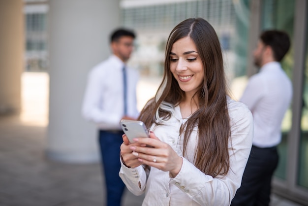 Junge Geschäftsfrau mit ihrem Smartphone vor ihrem Büro