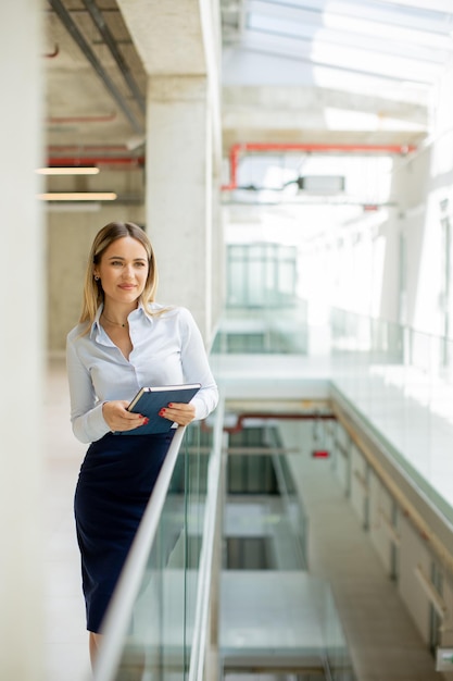 Foto junge geschäftsfrau mit notizbuch steht in der modernen bürowand